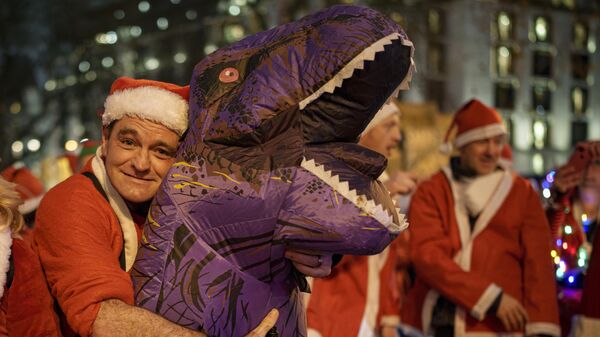 Мужчина в костюме Санта-Клауса обнимает свой надувной костюм динозавра в Лондоне, Великобритания - Sputnik Грузия