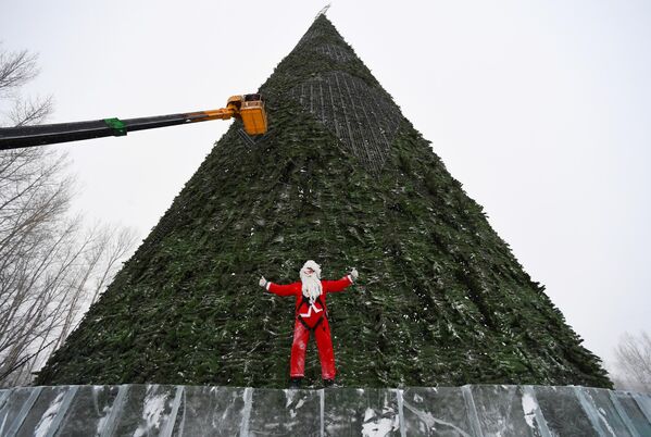 Промышленный альпинист в костюме Деда Мороза во время монтажа элементов светодинамической системы иллюминации 57-метровой главной городской елки на острове Татышев в Красноярске. - Sputnik Грузия