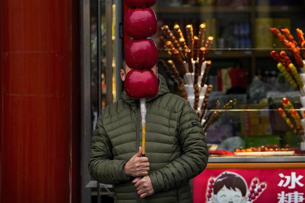 Продавец держит гигантский боярышник, покрытый сахаром, для привлечения покупателей возле своего магазина на пешеходной торговой улице Цяньмэнь в Пекине. - Sputnik Грузия