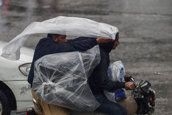 Водители на мотоцикле наматывают на себя полиэтиленовую пленку, чтобы укрыться от дождя в Пакистане. - Sputnik Грузия