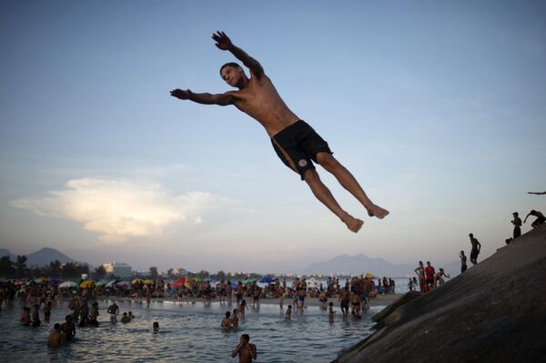 Мужчина прыгает со скалы в воду на пляже Рекрейо-дос-Бандейрантес во время изнуряющей жары в Рио-де-Жанейро. - Sputnik Грузия