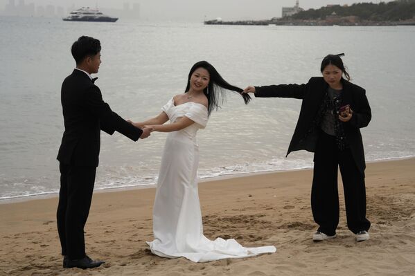 Женщина держит за волосы невесту, делая свадебные фотографии на пляже в Китае. - Sputnik Грузия