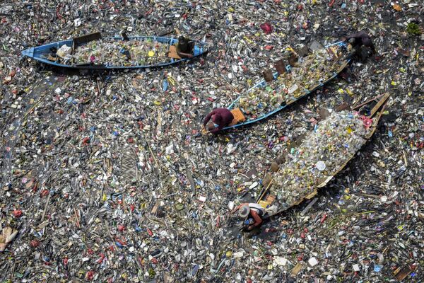 Люди на лодках собирают пригодный для вторичной переработки пластик из сильно загрязненной реки Читарум в Западной Яве. - Sputnik Грузия