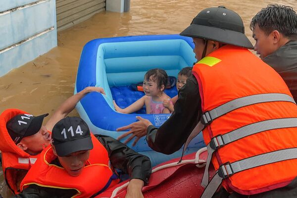 Спасатели помогают детям в надувной лодке выбраться из паводковых вод после сильного дождя в провинции Хазянг во Вьетнаме. - Sputnik Грузия
