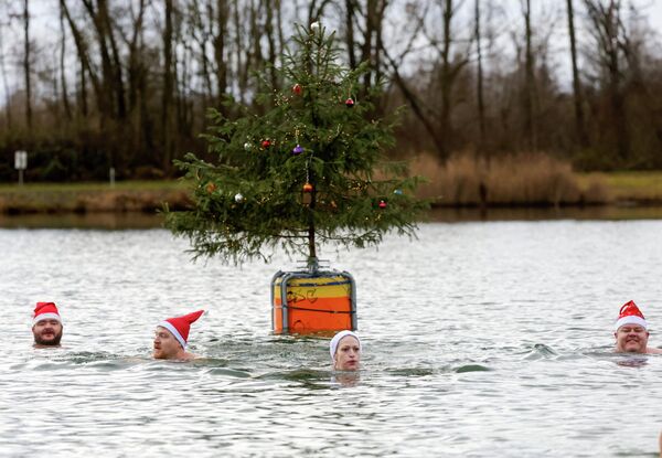 Мужчина и женщина в шапках Санта-Клауса купаются в озере, Германия. Мужчина и женщина в шапках Санта-Клауса купаются в озере, Германия. - Sputnik Грузия