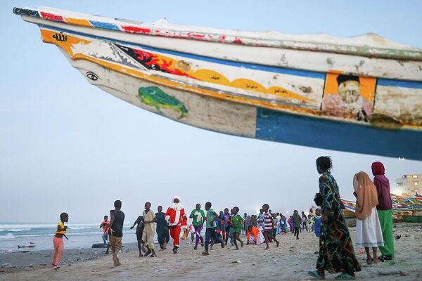 Санта-Клаус раздает подарки и сладости детям на пляже в бедном районе города Дакар в Сенегале. - Sputnik Грузия