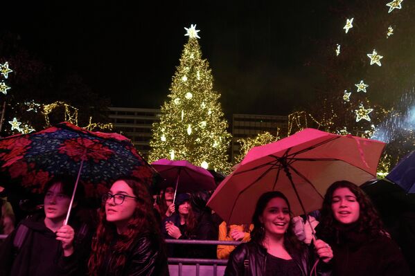 Публика слушает концерт под дождем в центре Афин на фоне сияющей рождественской елки. - Sputnik Грузия