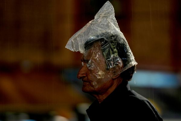 Мужчина, накрывающий голову полиэтиленовым пакетом, идет по улице под дождем в Хайдарабаде. - Sputnik Грузия
