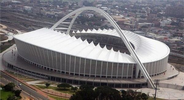 Durban Stadium (Дурбан Стэдиум), Дурбан.  Открытие: 2009 г. Вместимость: 69 957 зрителей. Транспорт: расстояние до аэропорта 35 км, железная дорога, автобус. Население города: 3 млн.  Еще один стадион, которому суждено принять полуфинал чемпионата. Внешний вид стадиона навеян очертаниями флага ЮАР. На стадионе, строительство которого обошлось в 450 миллионов долларов, имеется смотровая платформа, которая позволяет с высоты птичьего полета бросить взгляд на стадион и прилегающую к нему местность. Места были специально расположены таким образом, чтобы вне зависимости от сектора открывался хороший вид на происходящее на поле. Как и большинство стадионов, построенных специально к чемпионату миру, Дурбан Стэдиум планируется в дальнейшем использовать для проведения различных спортивных и развлекательных мероприятий. Будет проведен демонтаж трибун и сокращение вместимости до 54 тысяч. Комплекс стадиона включает в себя музей, поле, спортивный институт, транспортную станцию. Матчи: 13 июня - Германия - Австралия (группа D), 16 июня - Испания - Швейцария (группа H), 19 июня - Нидерланды - Япония (группа E), 22 июня - Нигерия - Южная Корея (группа B), 25 июня - Португалия - Бразилия (группа G), 28 июня - (1/8 финала), 07 июля - (1/2 финала). - Sputnik Грузия