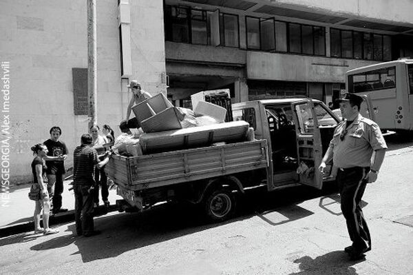Сотрудник полиции проходит мимо машины мэрии Тбилиси, на которой имущество выселяемых из здания издательства беженцев перевозится к их другому месту жительства. - Sputnik Грузия