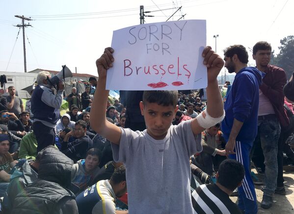 Мальчик держит плакат с надписью Сожалеем о Брюсселе в лагере беженцев на границе Греции и Македонии. - Sputnik Грузия
