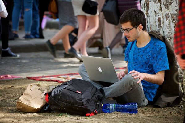 Молодой человек работает за ноутбуком, сидя на земле в парке. Тбилисский блошиный рынок. - Sputnik Грузия