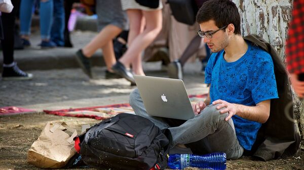 Молодой человек работает за ноутбуком, сидя на земле в парке. Хипстерский рынок - Sputnik Грузия