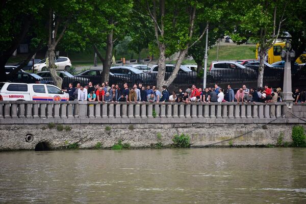 Люди, выстроившиеся вдоль перил на набережной, наблюдают за ходом проведения поисково-спасательной операция на реке Кура в Тбилиси. - Sputnik Грузия