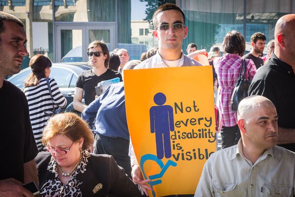 Участник шествия в защиту прав лиц с ОВЗ держит в руках плакат с надписью Не всякая инвалидность видна. - Sputnik Грузия