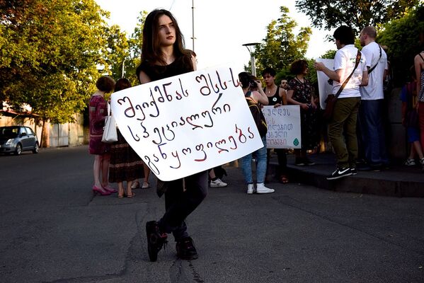Участница акции против семейного насилия стоит с плакатом лицом к сотрудникам полиции, которые дежурят у здания МВД. - Sputnik Грузия