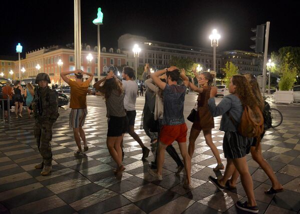 Люди пересекают улицу с поднятыми над головой руками, на месте теракта в Ницце. - Sputnik Грузия