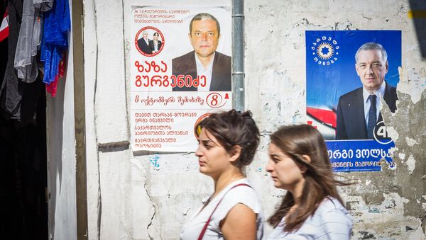 Женщины проходят мимо здания, на стене которого наклеены предвыборные плакаты - Sputnik Грузия