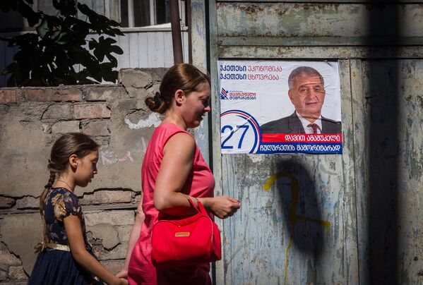Женщина с ребенком идет мимо здания, на стене которого наклеены предвыборные плакаты - Sputnik Грузия