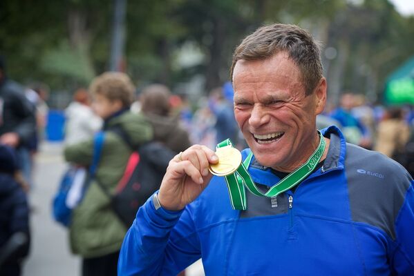 Участник марафона из Канады демонстрирует памятную медаль, полученную им после забега - Sputnik Грузия