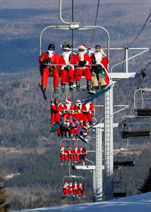 Лыжники и сноубордисты в костюмах Санты на горнолыжном курорте River Resort в американском штате Мэн поднимаются на склон горы, чтобы принять участие в благотворительном заезде - Sputnik Грузия