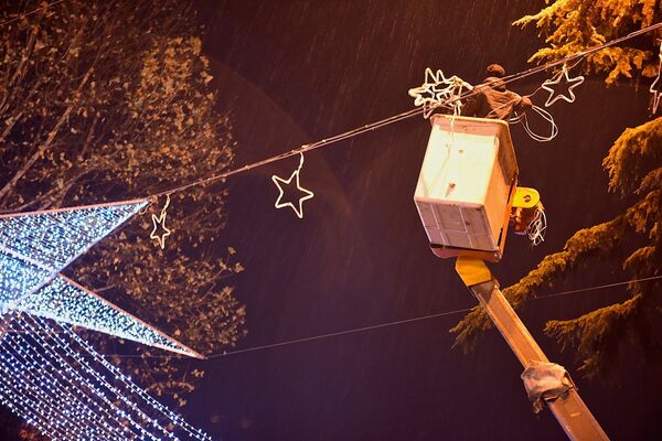 Рабочий развешивает новогодние фонарики над проспектом Руставели, в этот момент внизу проезжают машины - работы ведутся в вечернее время, когда улицы Тбилиси еще заполнены транспортом - Sputnik Грузия