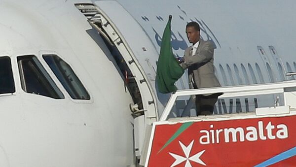 Один из угонщиков самолета Afriqiyah Airways машет ливийским флагом эпохи Кадаффи в аэропрту Мальты - Sputnik Грузия