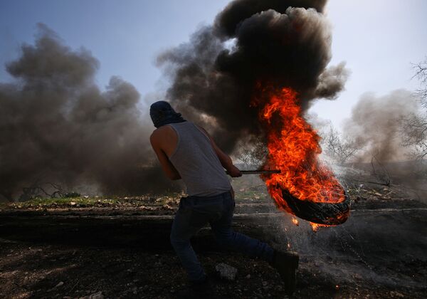 Палестинский демонстрант кидает горящую покрышку во время столкновений с израильскими войсками недалеко от Наблуса, на границе Сектора Газа - Sputnik Грузия