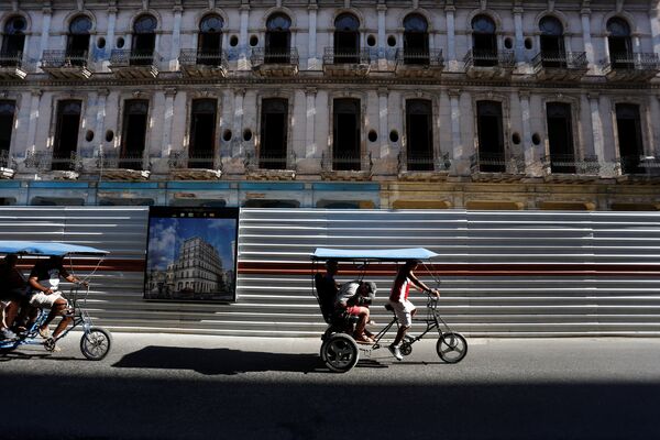 Велотакси проезжают мимо исторического здания, в котором проходят реставрационные работы в Гаване, Куба. Велорикши - это недорогой и очень распространенный в кубинской столице вида общественного транспорта - Sputnik Грузия