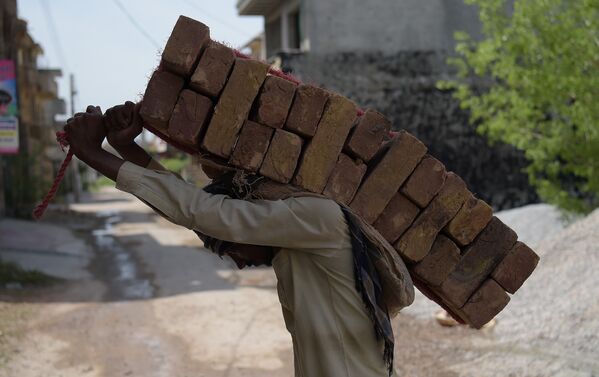 Пакистанский рабочий несет кирпичи на спине на строительной площадке в жилом районе в Исламабаде - Sputnik Грузия