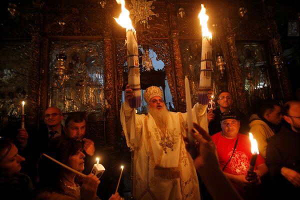Глава греческой православной церкви Рождества Христова в Вифлееме епископ Феофилактос держит в руках свечи, освещенные Благодатным огнем после его прибытия из Храма Гроба Господня, расположенном в Иерусалиме - Sputnik Грузия