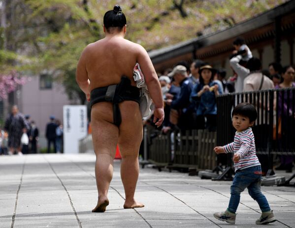Мальчик идет рядом с борцом сумо мимо зрителей в усыпальнице Ясукуни в Токио. Лучшие борцы сумо приняли участие в ежегодной однодневной выставке для тысяч зрителей в стенах храма - Sputnik Грузия