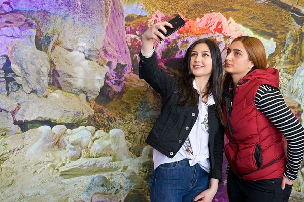 Девушки фотографируются у стенда с изображением Пещеры Прометея на Международной туристической выставке в столице Грузии - Sputnik Грузия
