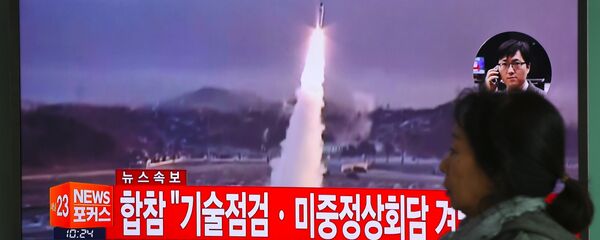 Женщина проходит мимо телевизионного экрана, показывающего видеозапись запуска ракеты Северной Кореей, на железнодорожной станции в Сеуле - Sputnik Грузия