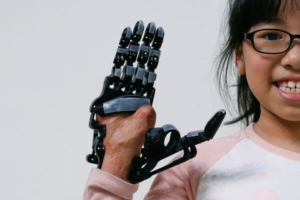 Восьмилетняя девочка, которая получила травму в результате аварии, показывает напечатанный на 3D-принтере протез руки, разработанный и построенный инженером Чанг Сянь-Лян, в Таоюань, Тайвань - Sputnik Грузия