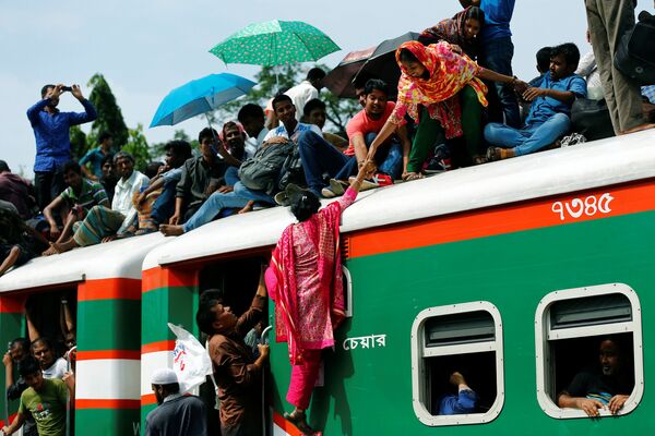 Люди помогают женщине взобраться на переполненный пассажирский поезд, когда они отправляются домой, чтобы отметить мусульманский праздник Ид аль-Фитр на железнодорожной станции в Дакке, Бангладеш - Sputnik Грузия