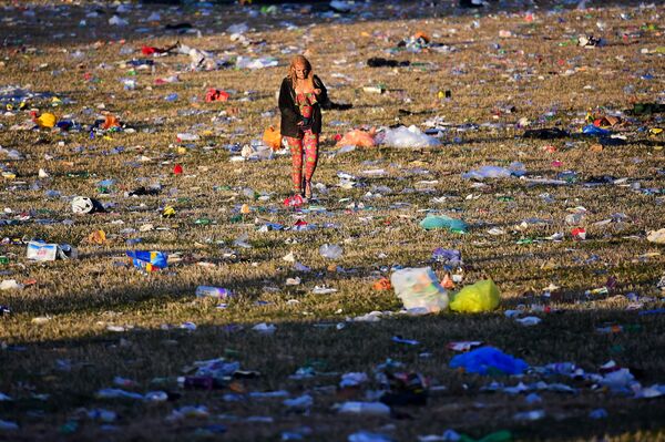 Девушка гуляет по полю, заваленному мусором, в Сомерсете во время фестиваля Glastonbury в Великобритании - Sputnik Грузия
