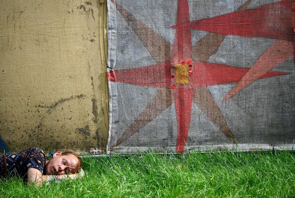 Молодой человек спит на траве во время Фестиваля Glastonbury в Великобритании - Sputnik Грузия