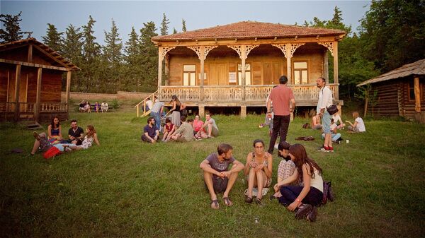 Люди отдыхают, сидя на земле на территории Этнографического музея летним вечером в Тбилиси - Sputnik Грузия