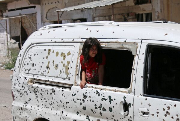 Девочка смотрит из разбитого окна автобуса, весь кузов которого изрешечен пулями, в Сирии - Sputnik Грузия