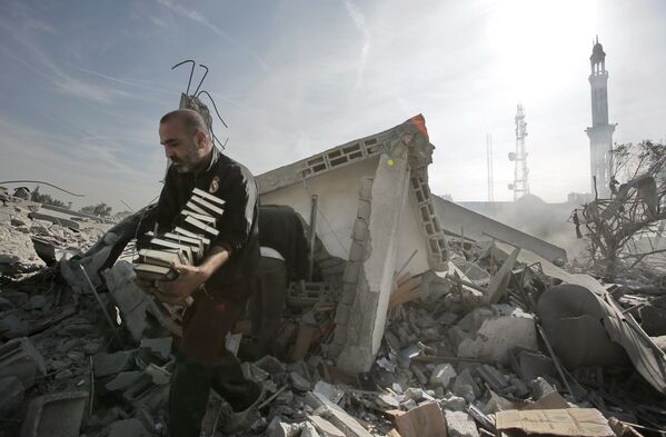 Мужчина выносит стопки Корана из разрушенного взрывом здания в Газе, 2012 год - Sputnik Грузия
