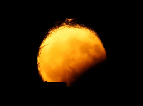 Вид Луны во время частичного лунного затмения искажается горячим воздухом, поднимающимся из дымовых труб электростанции в Делимаре, за пределами деревни Марсаклокк, Мальта - Sputnik Грузия