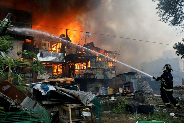 Пожарный тушит на лачуги, охваченные пламенем во время пожара в жилом районе Кесон-Сити, Филиппины - Sputnik Грузия