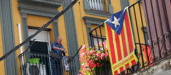 Мужчина развешивает одежду на балконе на севере Барселоны, на фоне флага Каталонии - Sputnik Грузия