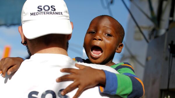 Член экипажа организации SOS Mediterranee с ребенком после спасения группы мигрантов во время операции поиска и спасения (SAR) в Средиземном море от Ливийского побережья - Sputnik Грузия