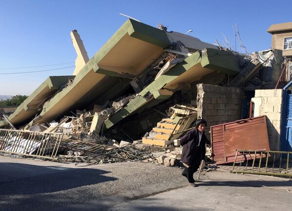 Сотни человек погибли и десятки тысяч лишились крова в результате сильного землетрясения, которое произошло на границе Ирака и Ирана. На фото - человек проходит мимо разрушенного здания в городе Дарбандихан в Ираке - Sputnik Грузия