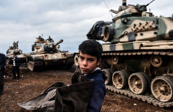 Маленький житель Турции стоит рядом с танками турецкой армии во время концентрации ударных сил близ сирийской границы в провинции Хатай. Турецкие войска 20 января 2018 года начали военную операцию на территории Сирии против курдских формирований - Sputnik Грузия