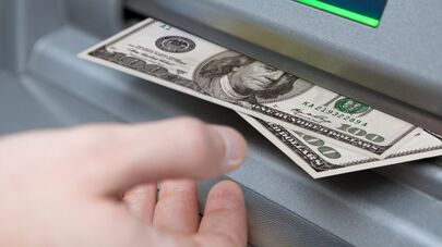 Мужчина берет купюры долларов из банкомата