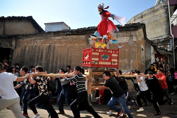 Деревенские жители несут на руках носилки с одетыми в традиционные национальные костюмы детьми. Это парад вокруг деревни, когда местные жители отмечают традиционный народный обряд Цугуши, празднуя Фестиваль китайских фонарей в районе Лонгьян, провинция Фуцзянь, Китай - Sputnik Грузия