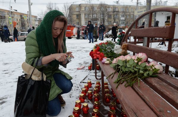 Женщина зажигает свечу возле здания торгового центра Зимняя вишня в Кемерово в память о погибших в результате пожара - Sputnik Грузия